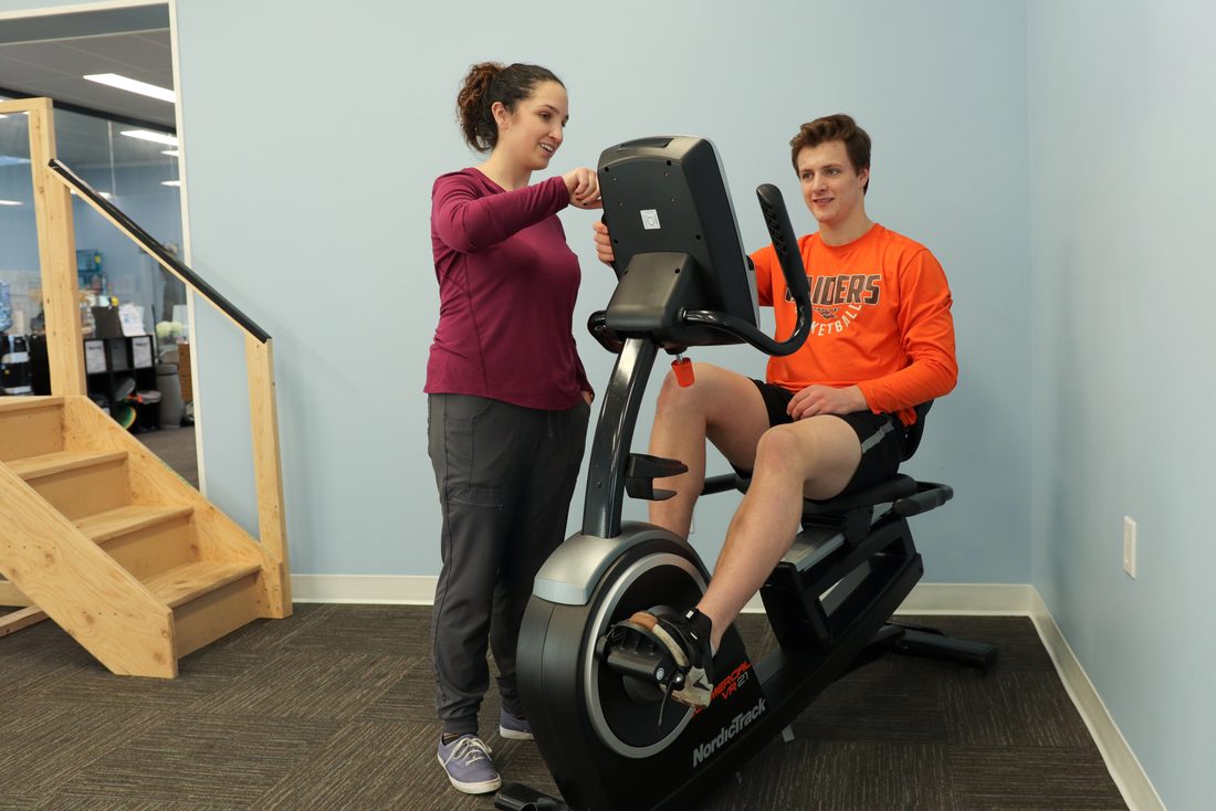 Physiotherapist guiding a patient through recumbent-bike rehabilitation after surgery