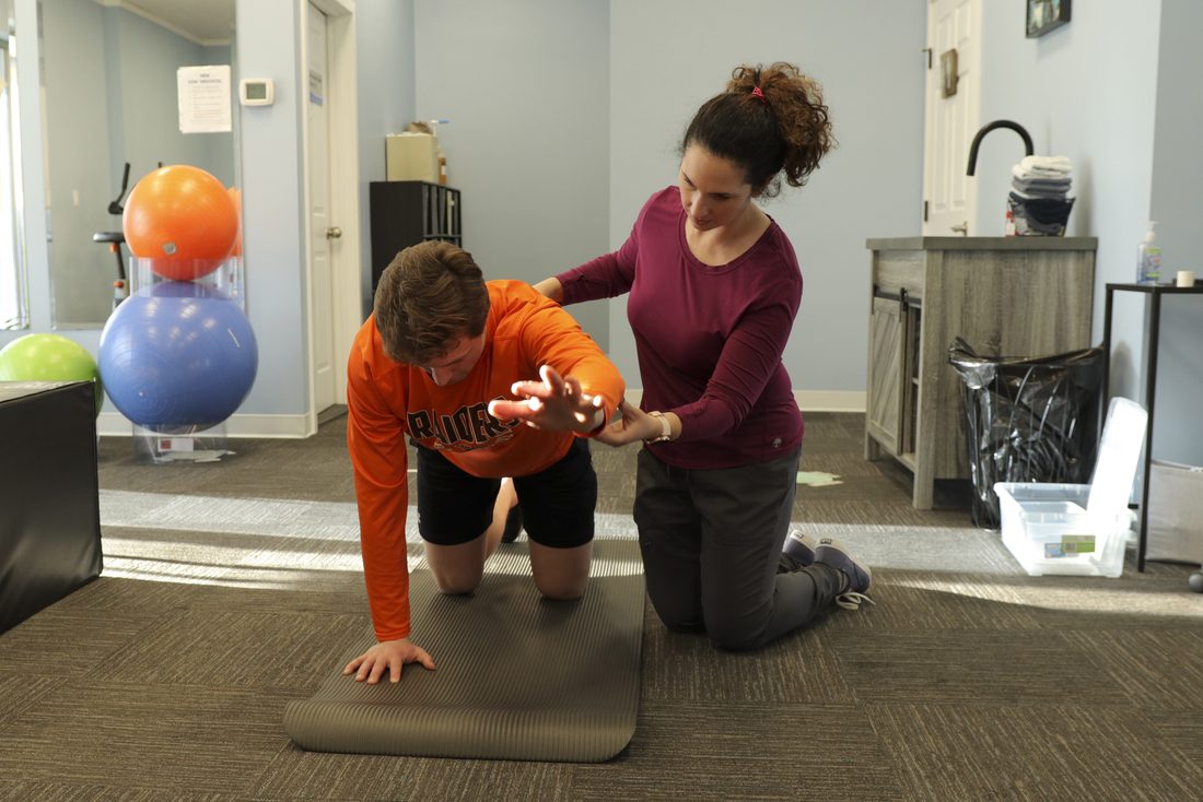 Physiotherapist guiding a patient through a core stability exercise on a mat